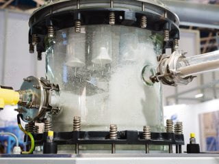 Transparent industrial hopper showing powdered material flowing through a processing system